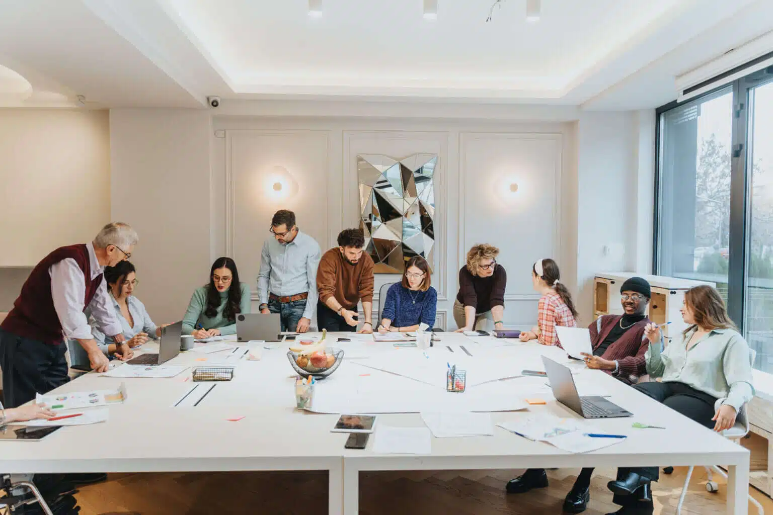 Team arbeitet in einem Workshop gemeinsam an einem großen Tisch mit Laptops und Unterlagen